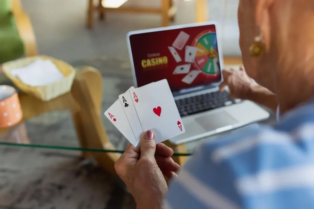 Person playing online casino on laptop while holding aces cards